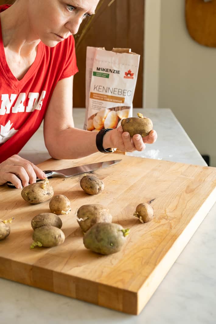 Karen Bertelsen stands at a counter with a cutting board covered in seed potatoes.