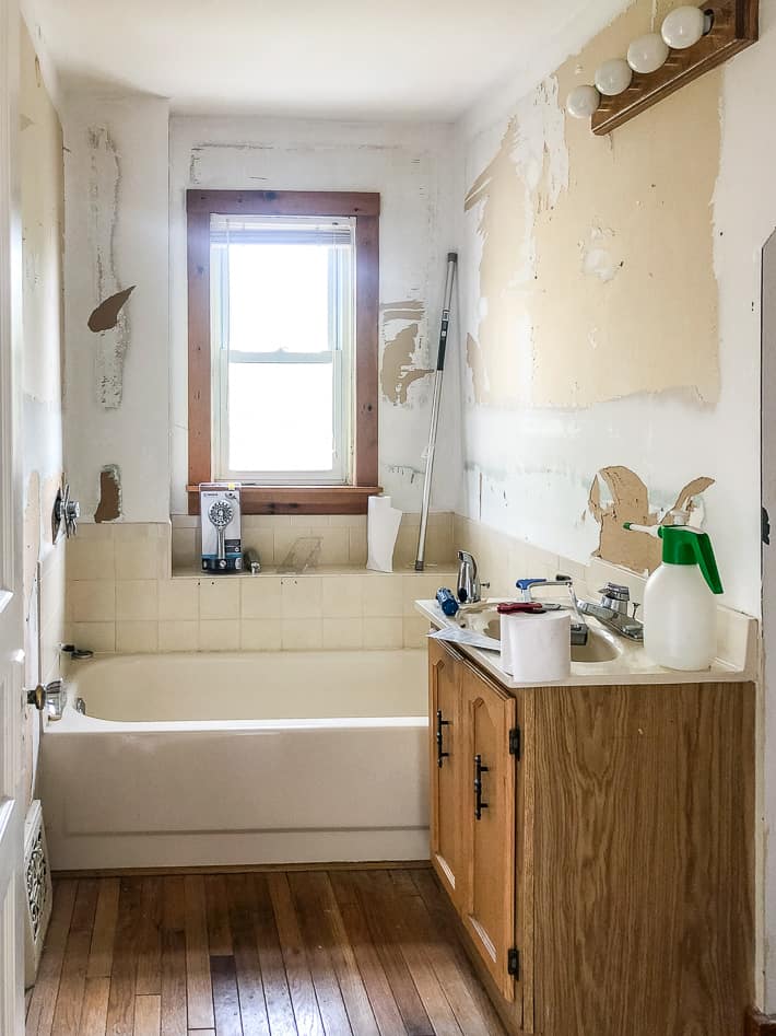 Older bathroom mid renovation with mangled walls, an old oak vanity and no shower.