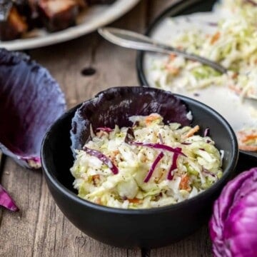 Classic coleslaw in a black bowl on wood table.