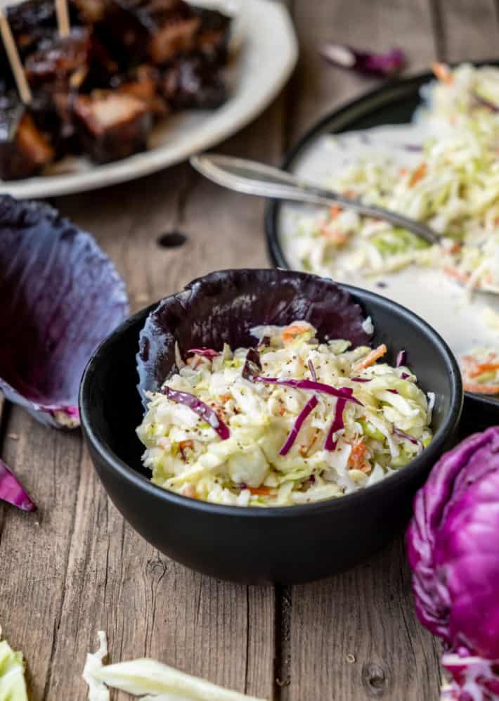 Classic coleslaw in a black bowl on wood table.