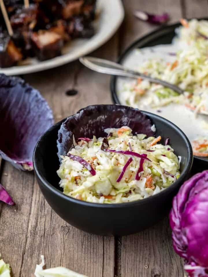 Classic coleslaw in a black bowl on wood table.