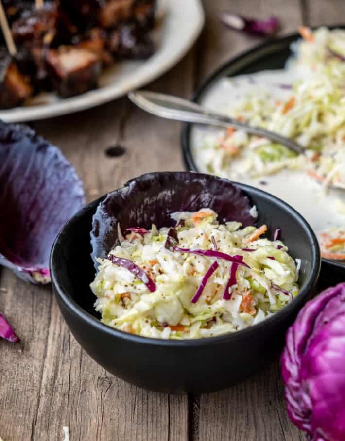 Traditional coleslaw in a small black bowl lined with a red cabbage leaf.