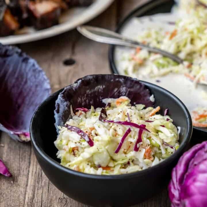 Traditional coleslaw in a small black bowl lined with a red cabbage leaf.
