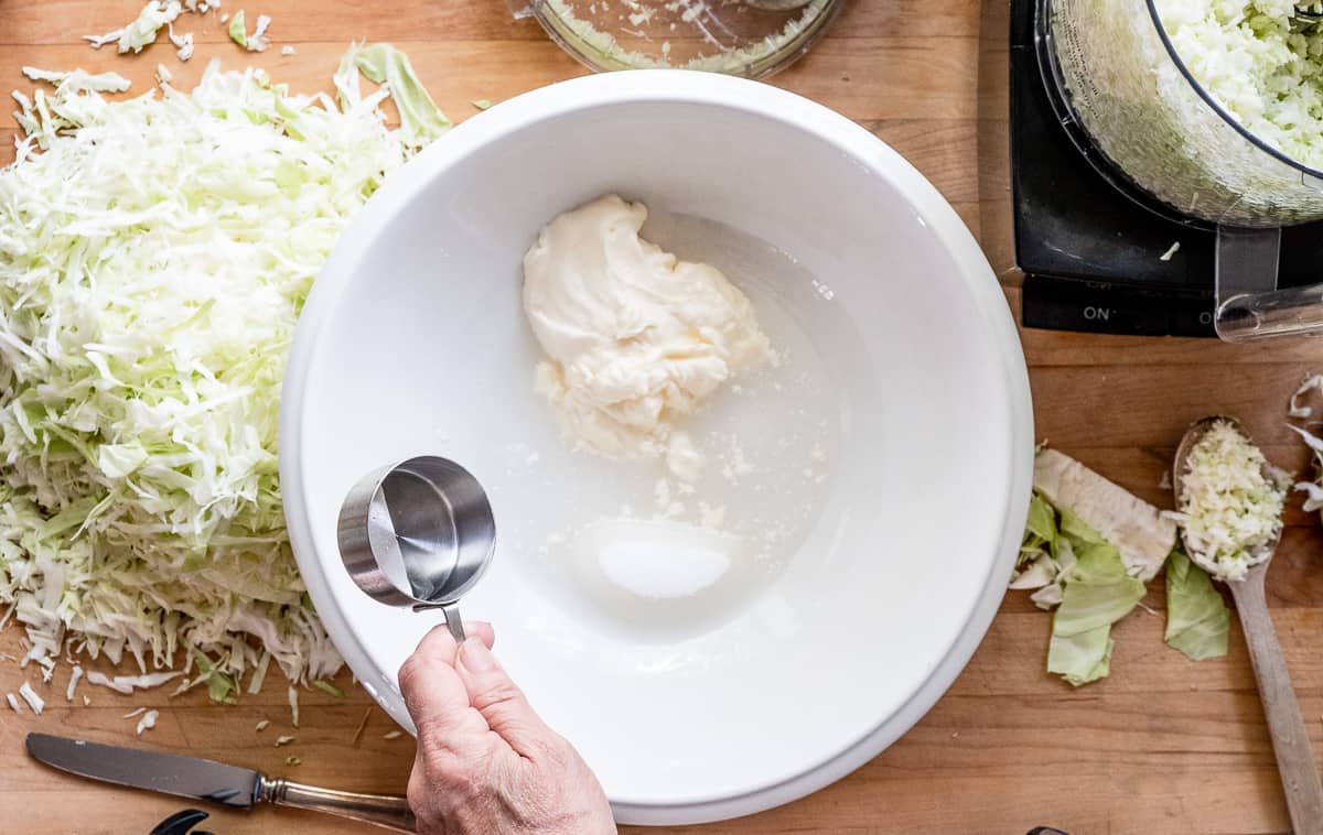 Adding vinegar to ironstone bowl containing sugar, mayo, salt and water.