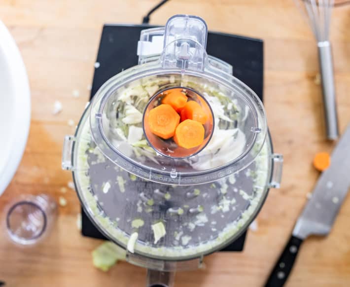 Carrots being fed through the tube of a Cuisinart food processor seen from above.