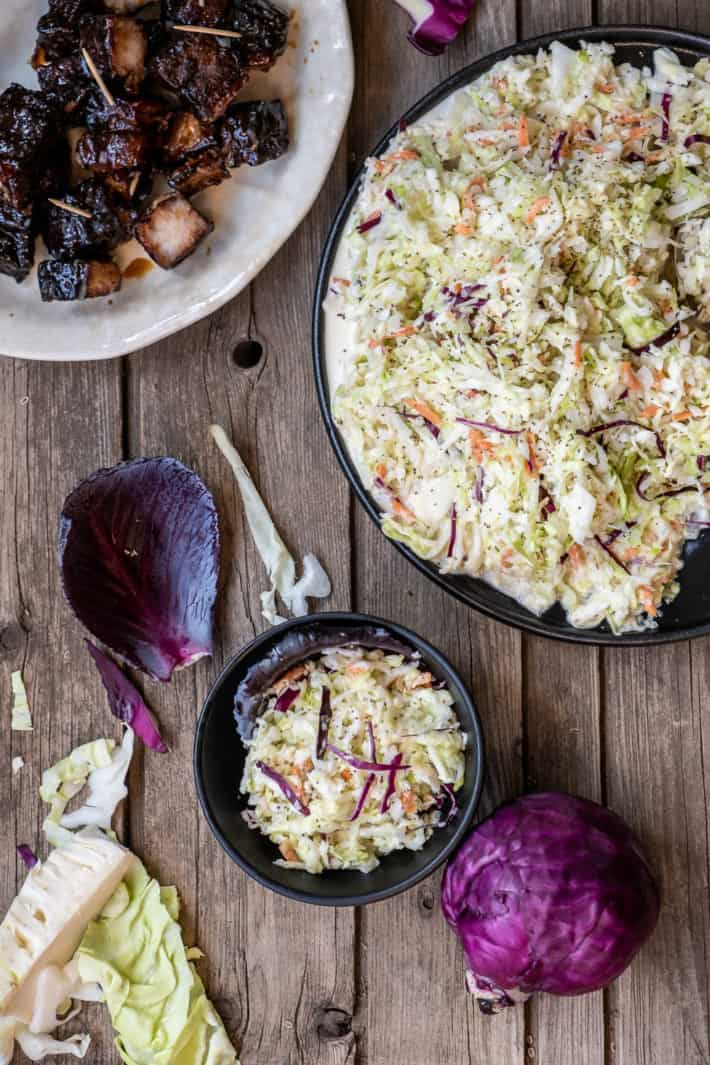 Overhead view of a wood table covered with plates filled with smoked pork belly and colourful slaw.