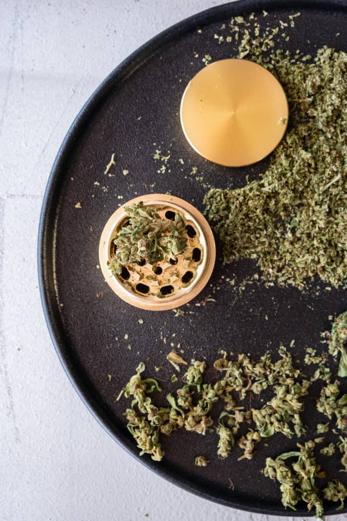 Gold herb grinding surrounded by ground cannabis.