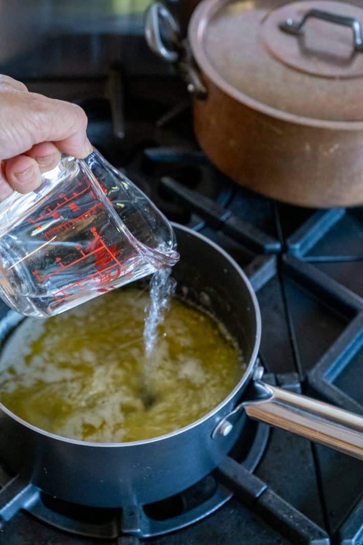 1 cup of water being poured into 1 cup of melted butter in a pot on the stove.