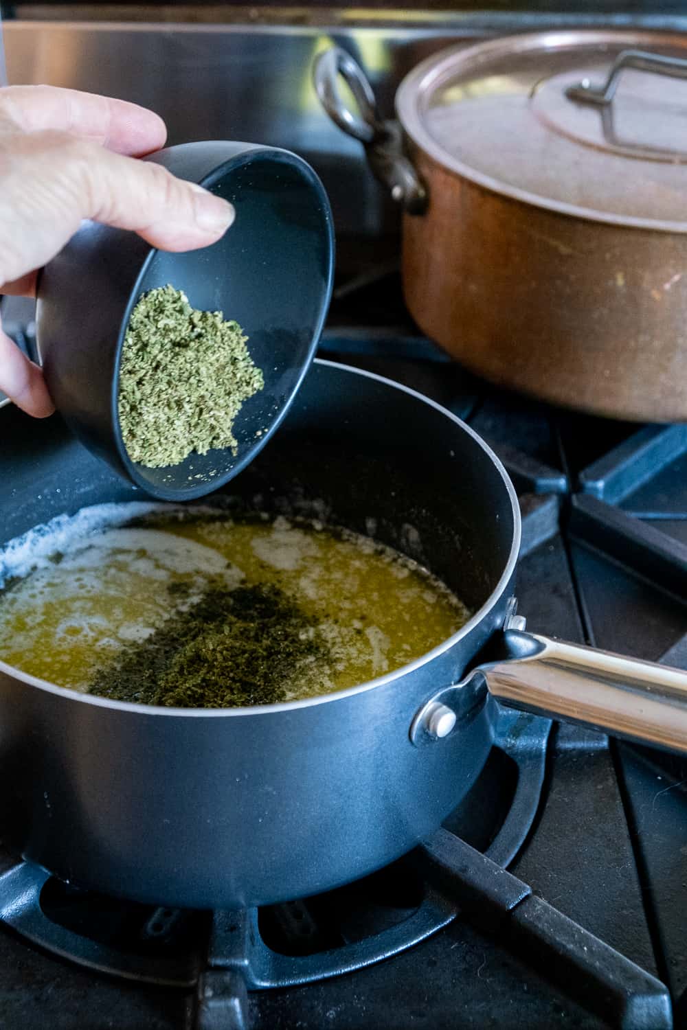 Decarbed, ground cannabis being dropped from black bowl into pot of butter and water.