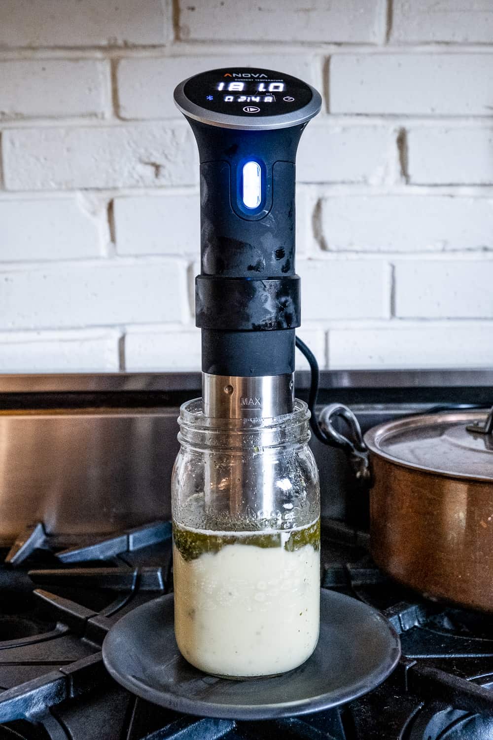 A sous vide stick in a mason jar being used to infuse cannabutter showing a temperature of 180 F.
