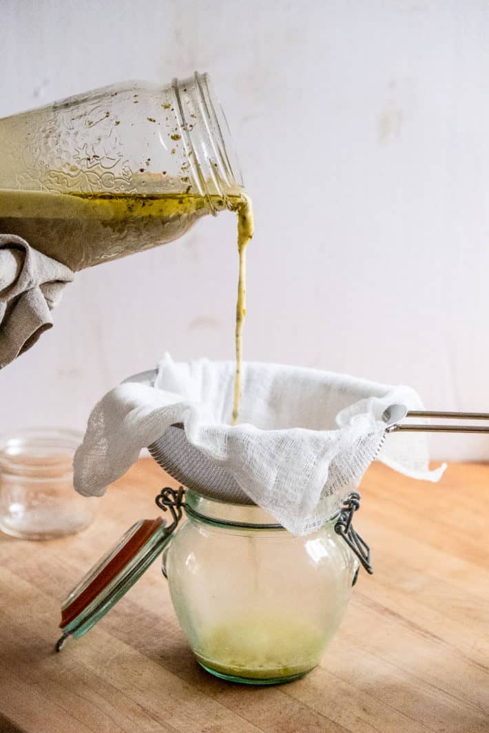 Pouring a green tinged cannabis infused butter out of a mason jar and into cheesecloth.