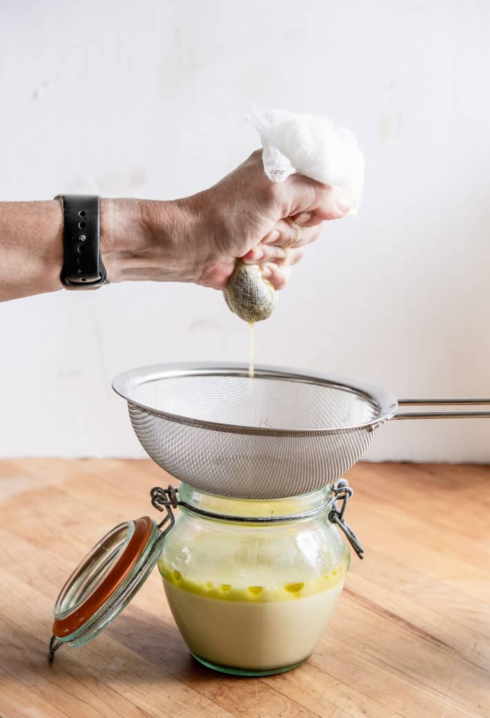 Squeezing a ball of cannabis and butter filled cheesecloth over a strainer.