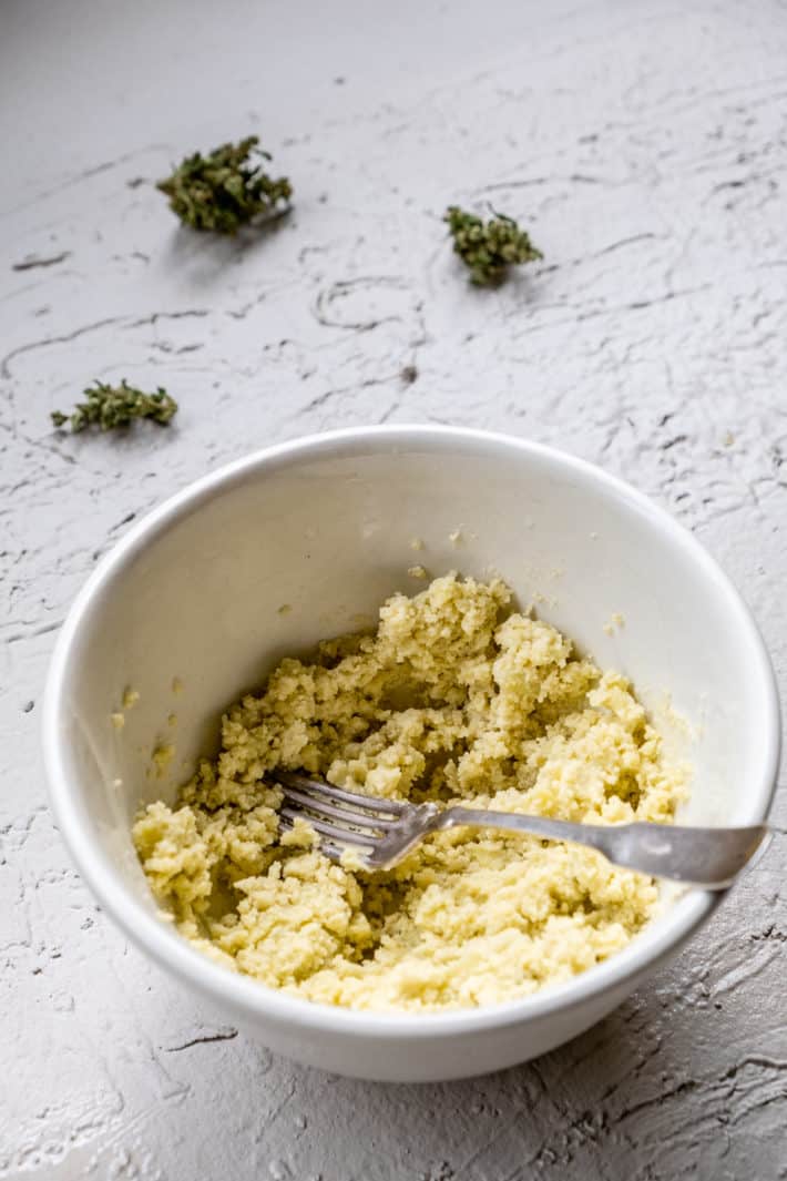Cannabutter in a white ironstone bowl being mashed with a fork.