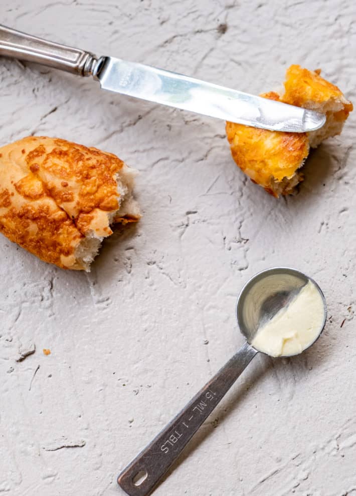 A vintage knife rests on one of two pieces of cheese bread with a half teaspoon of cannabutter in front.