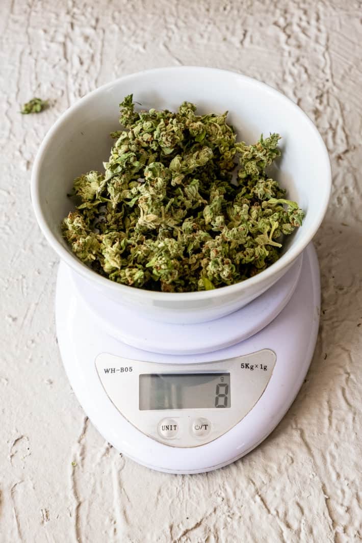 White digital scale on white table, weighing out 8 grams of cannabis.