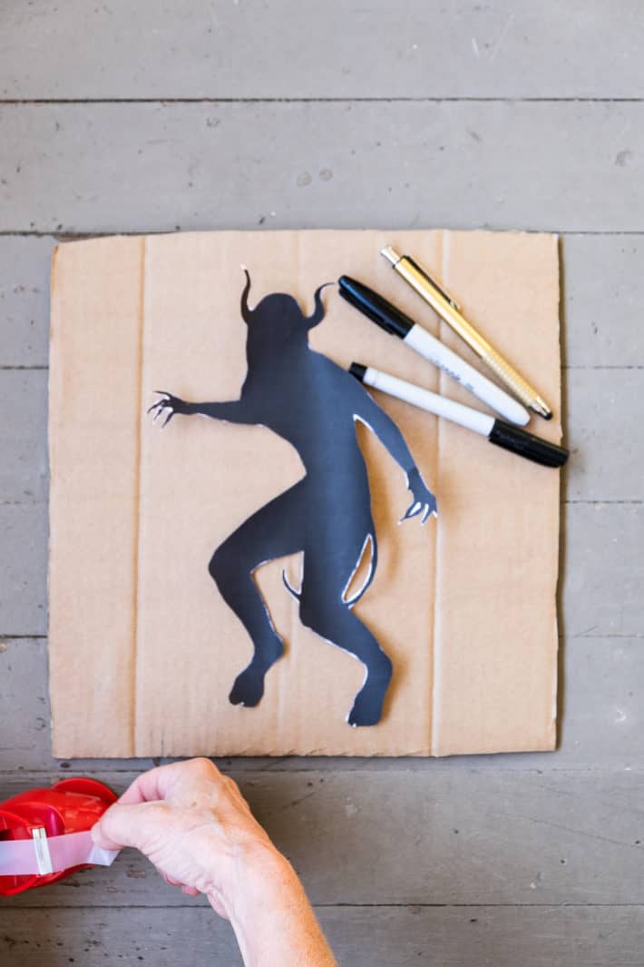 Demon silhouette printed and cut out sitting on cardboard with pens.