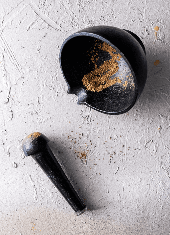 Freshly ground cumin seeds in black cast iron mortar with pestle to the side. 