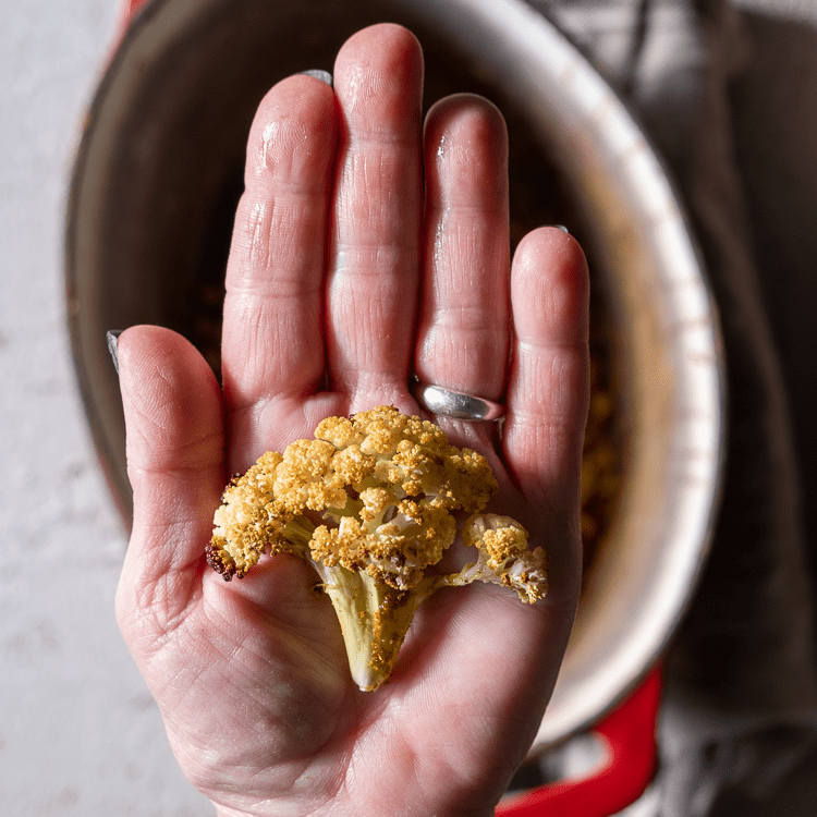 Slice of roasted cauliflower held in the palm of a hand.