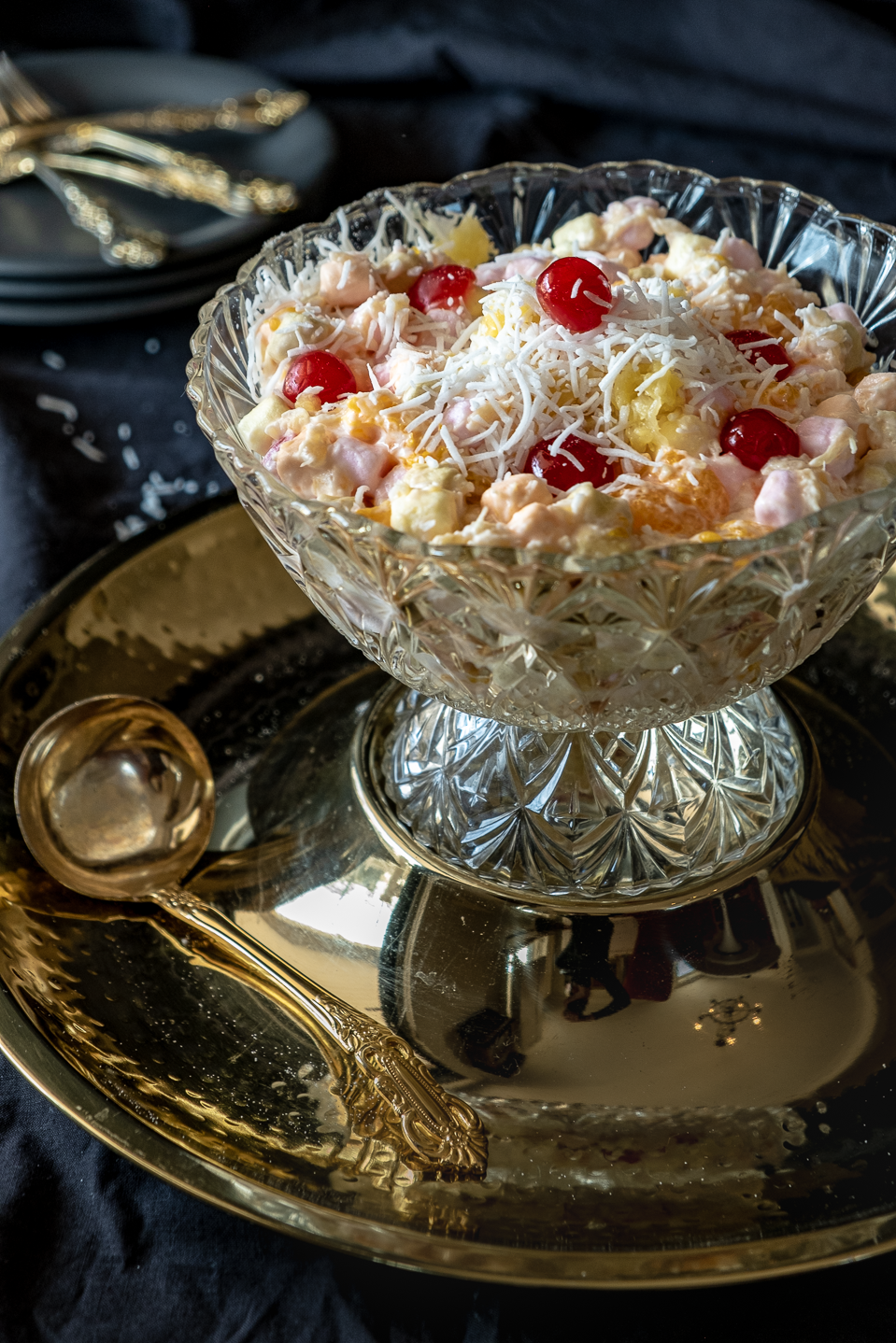 Marshmallow Salad topped with coconut and maraschino cherries in a cut glass bowl.