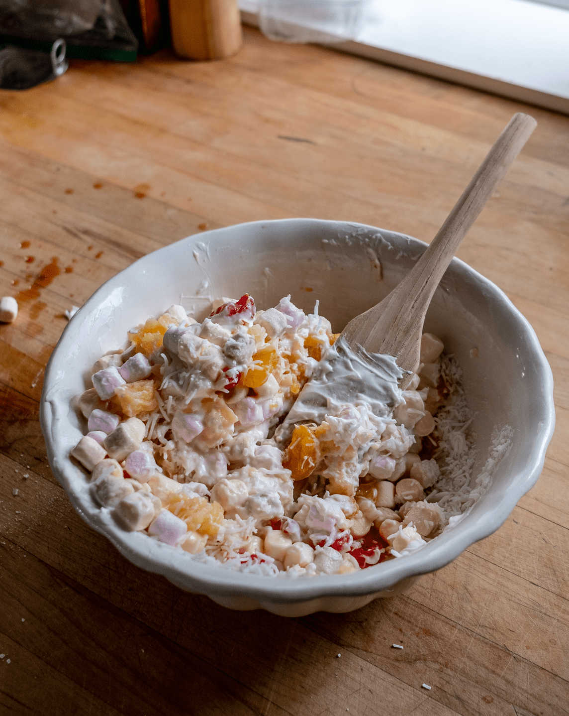 Folding ingredients of marshmallow salad in an ironstone bowl.