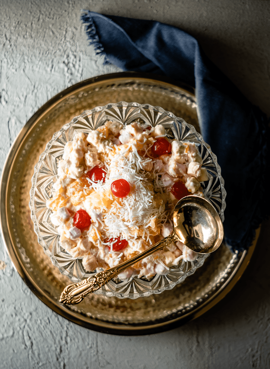 Marshmallow Salad topped with coconut and maraschino cherries in a cut glass bowl.