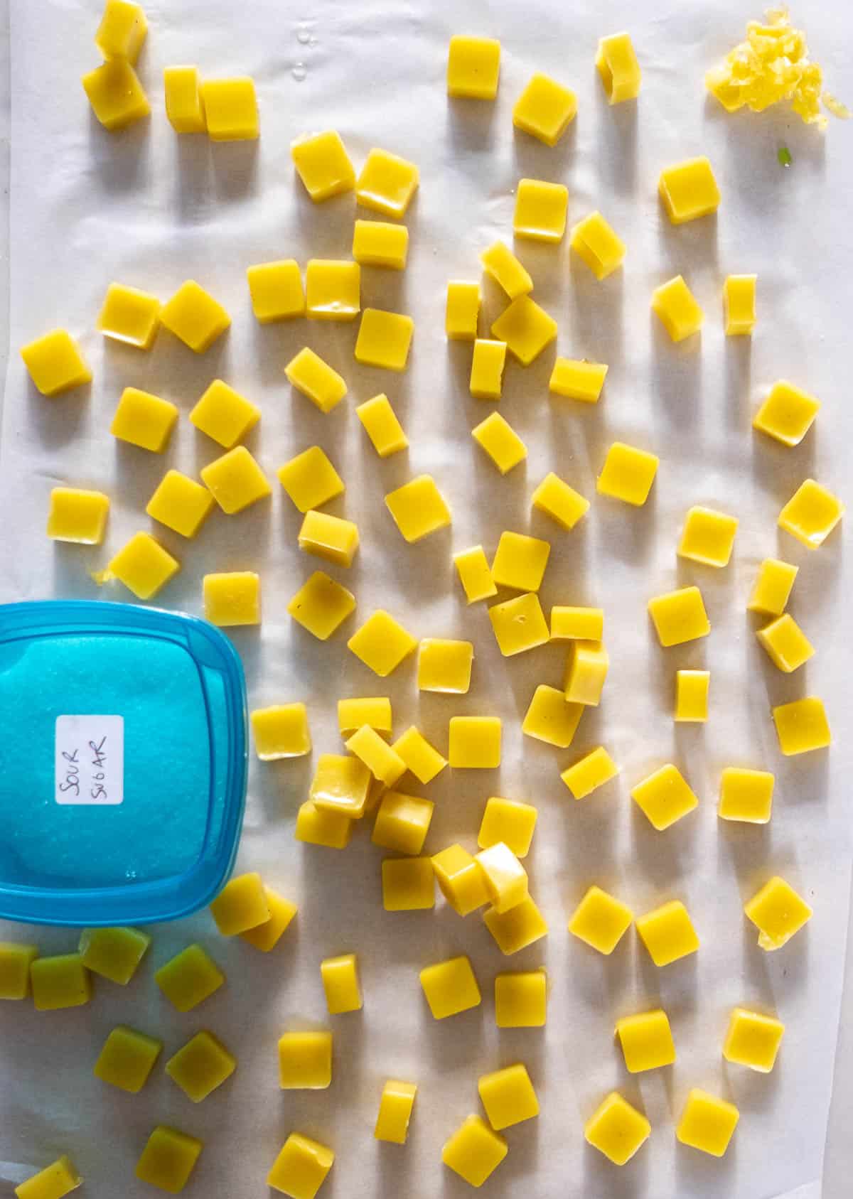 Bright yellow CBD gummies with a container of sour sugar.