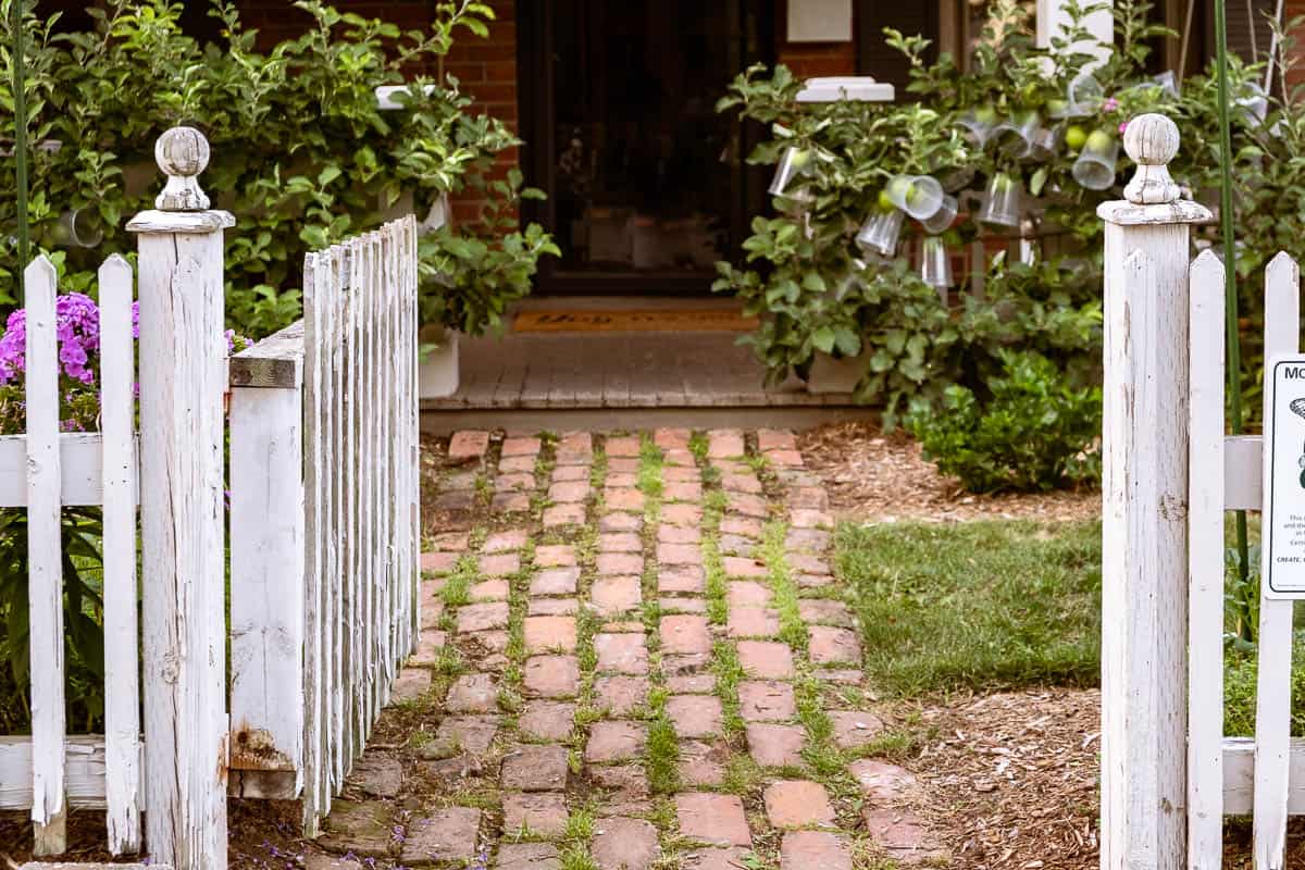 White picket fence with gate open leading to a brick pathway.