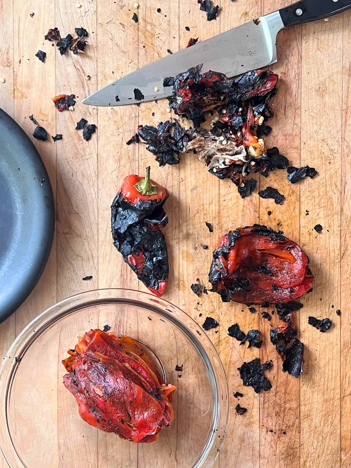 Red peppers on butcher block countertop at various stages of preparation after charring.