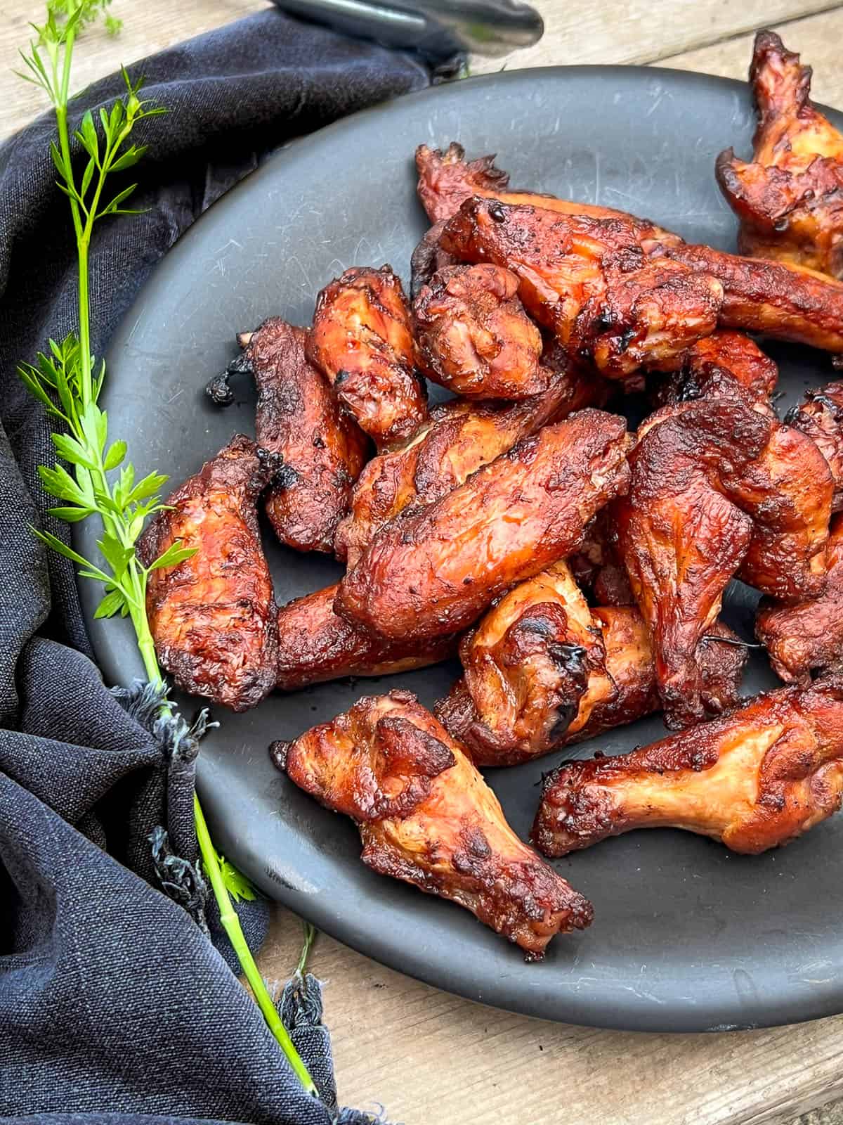 Smoked wings on a black plate with a green garnish.