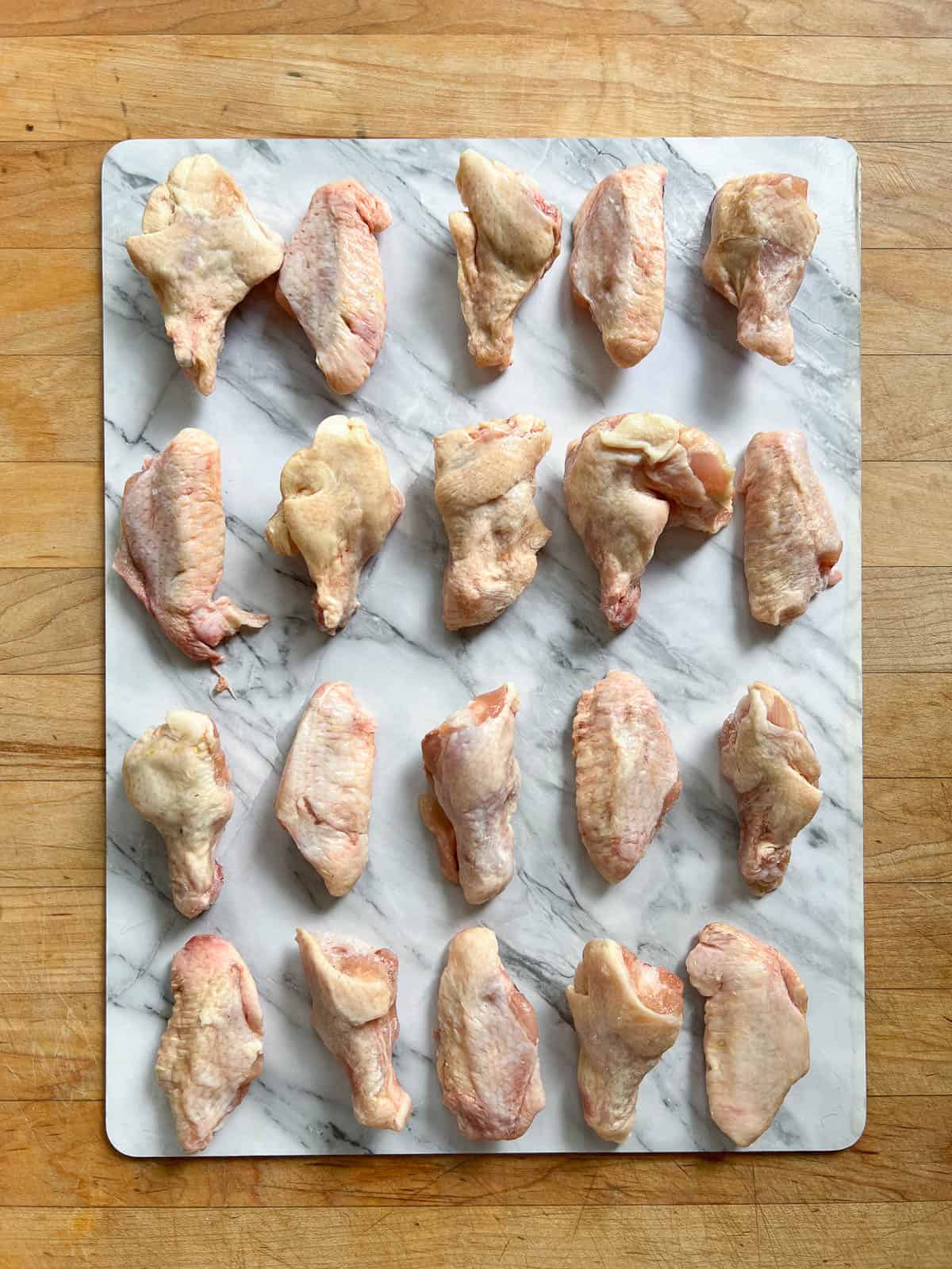 Raw chicken wings laid out in rows on a marble slab.