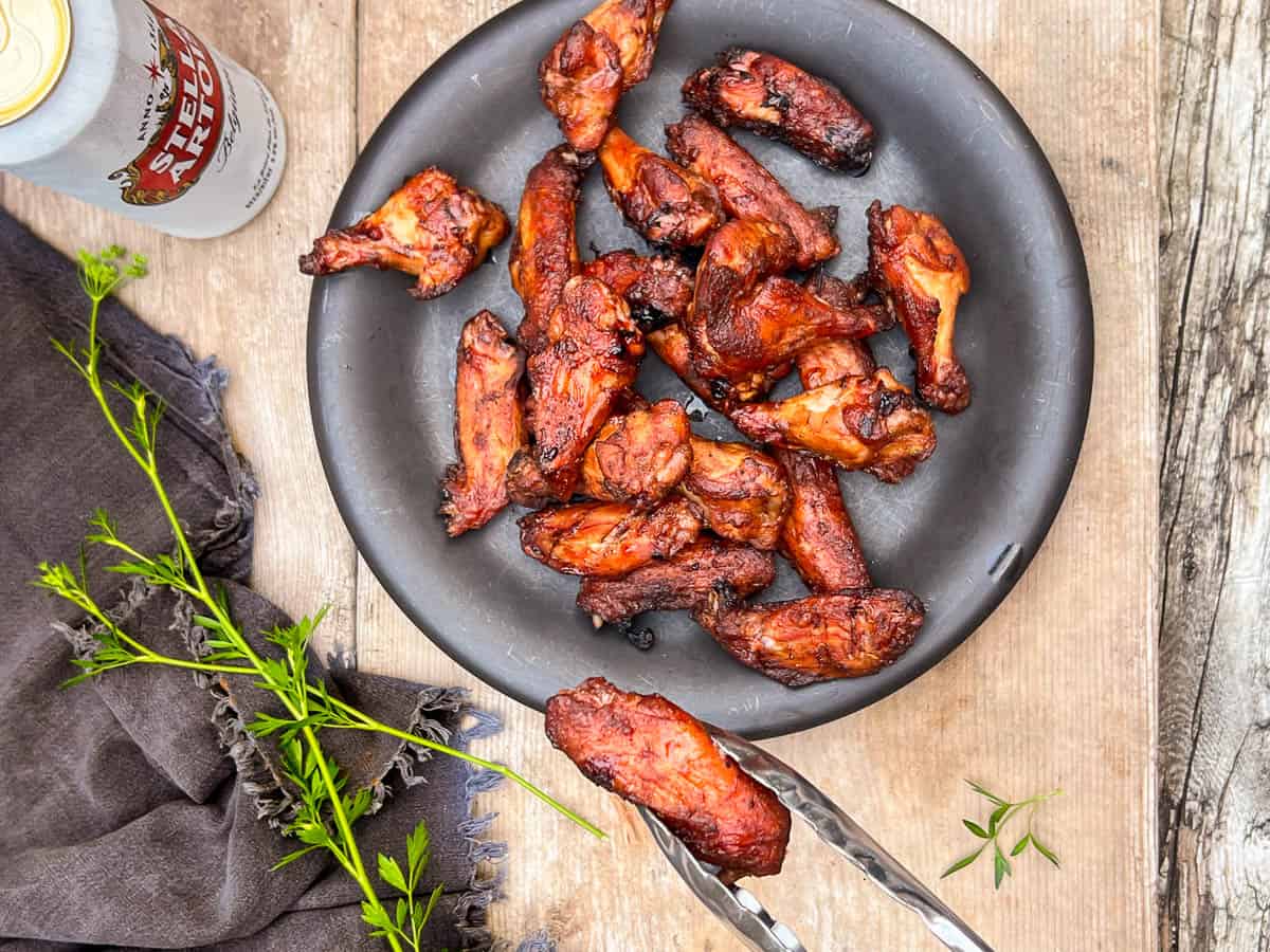 Smoked wings on a black plate with beer to the side.