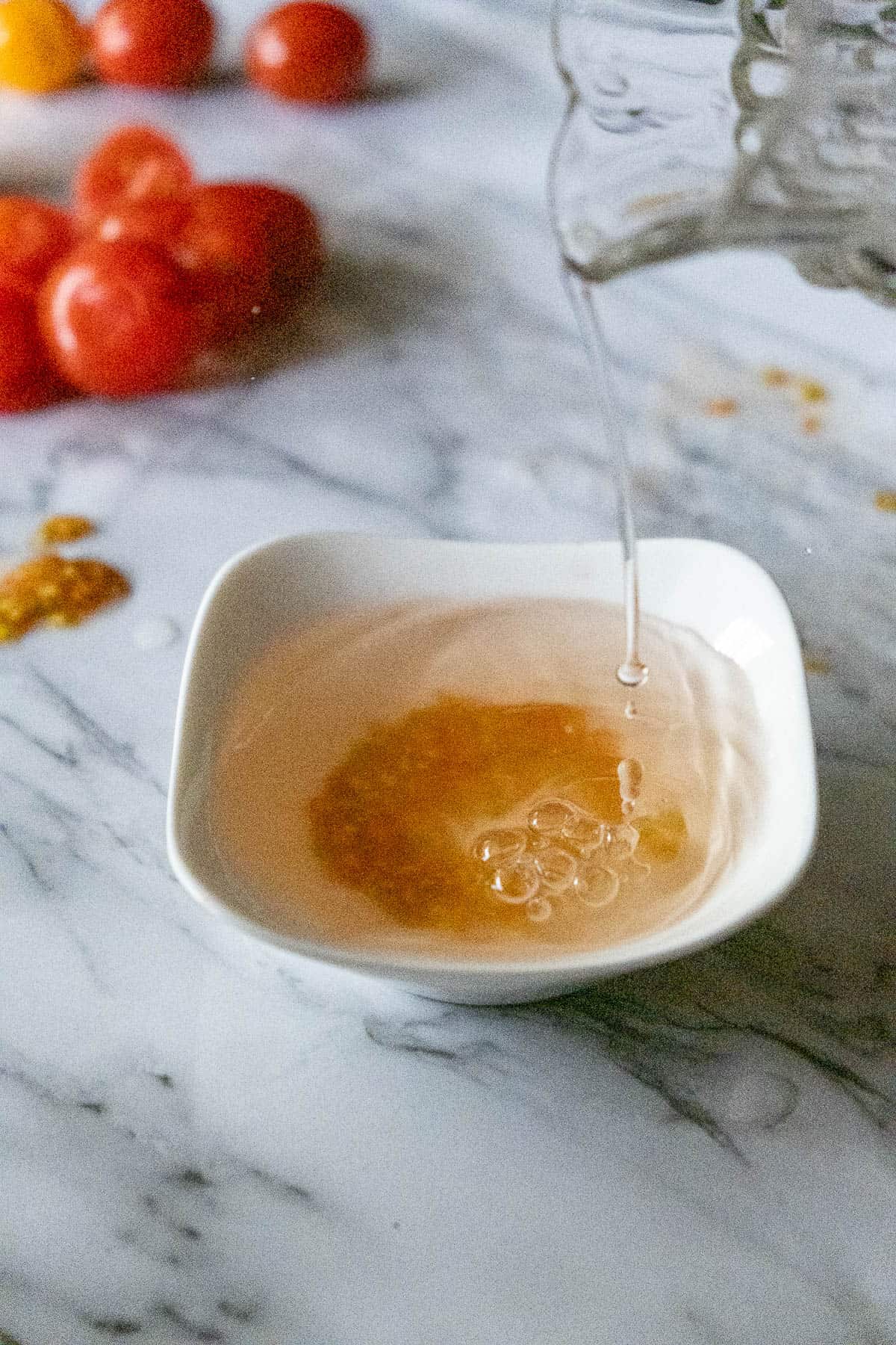 Water pouring from a glass jug into a small bowl with tomato seeds.