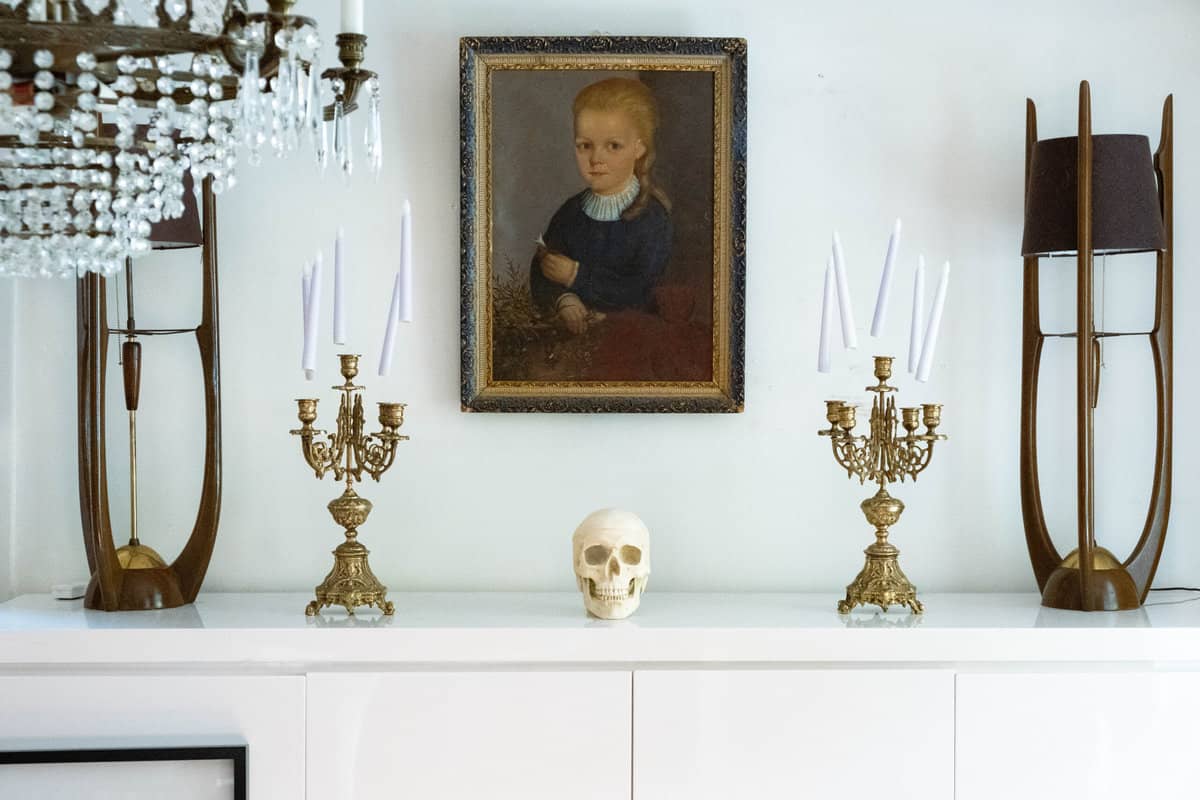 Creepy child portrait over white buffet with midcentury modern lamps and haunted floating candles over candelabras.