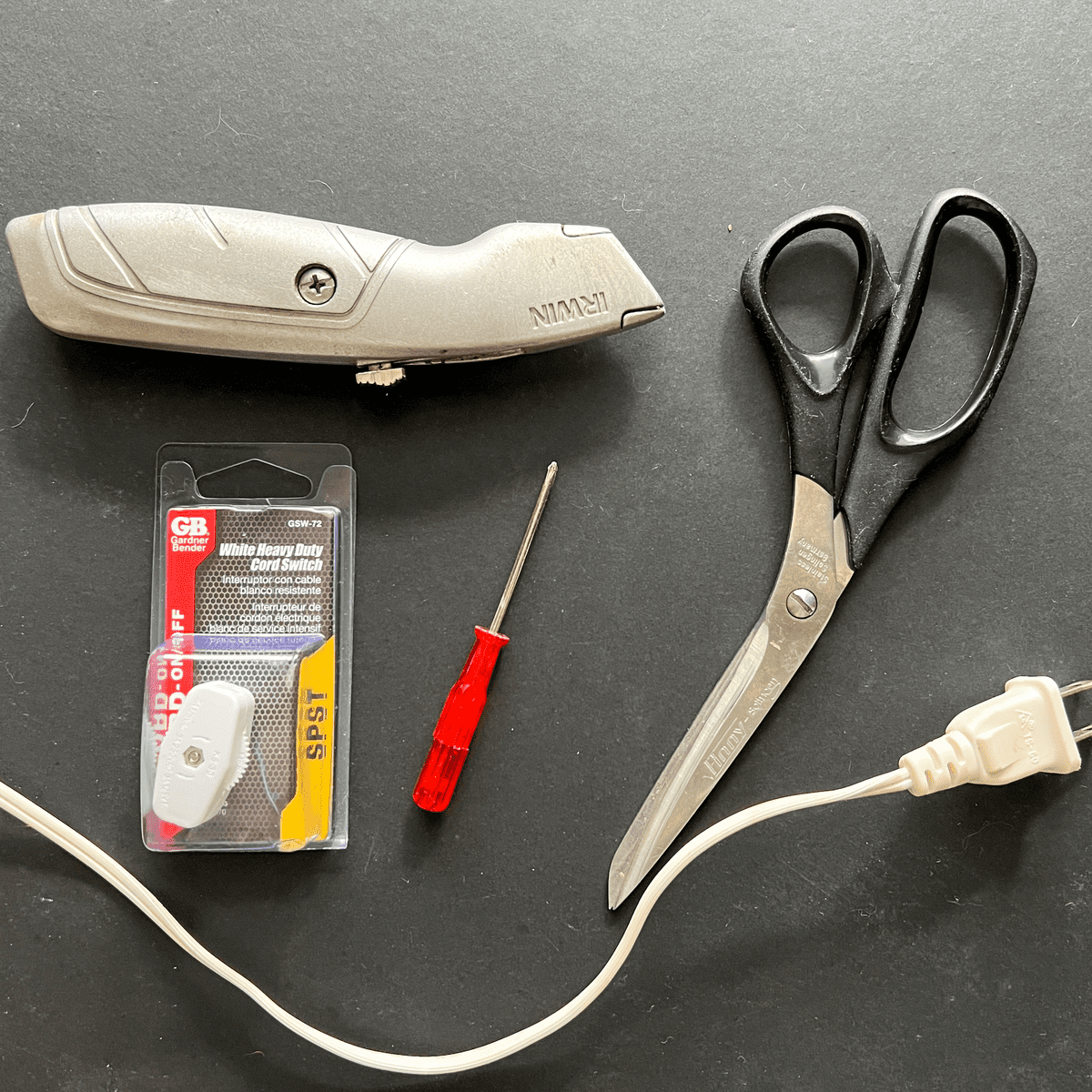Box cutter, black handled pair of scissors, cord with plug, mini screwdriver and light switch.