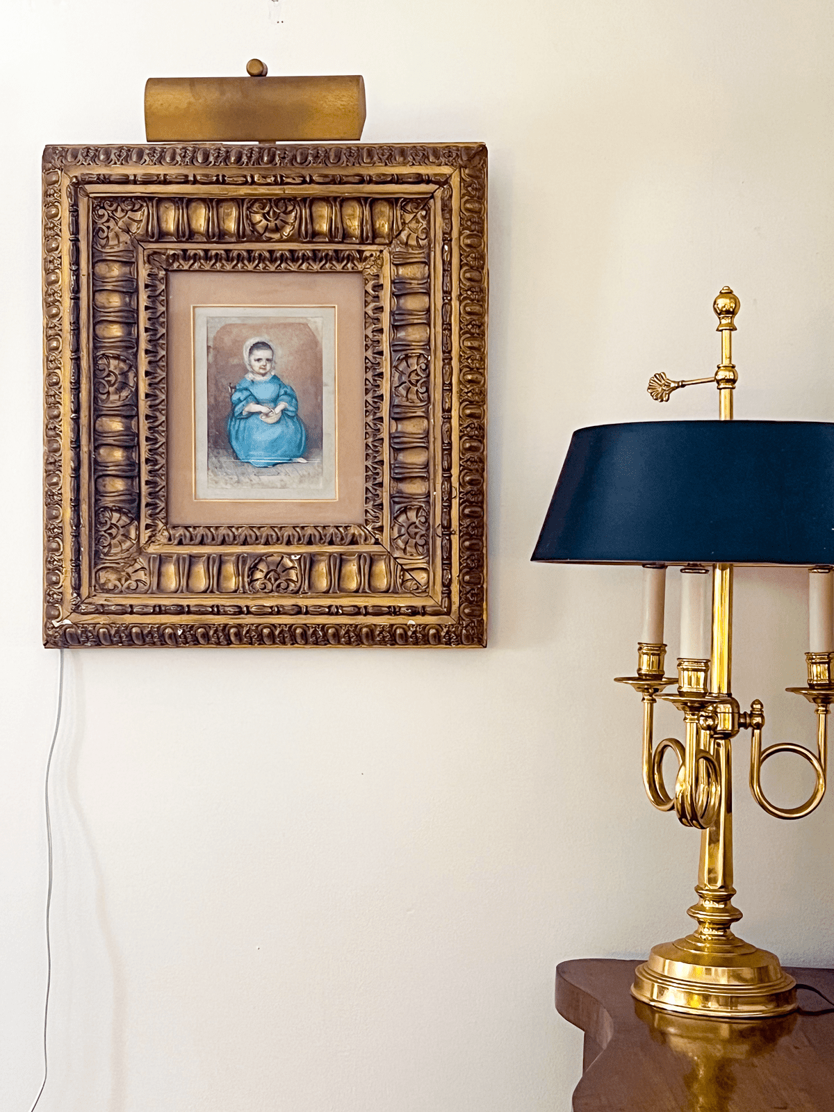 Ornate antique gold frame on wall with traditional brass lamp with black lampshade.