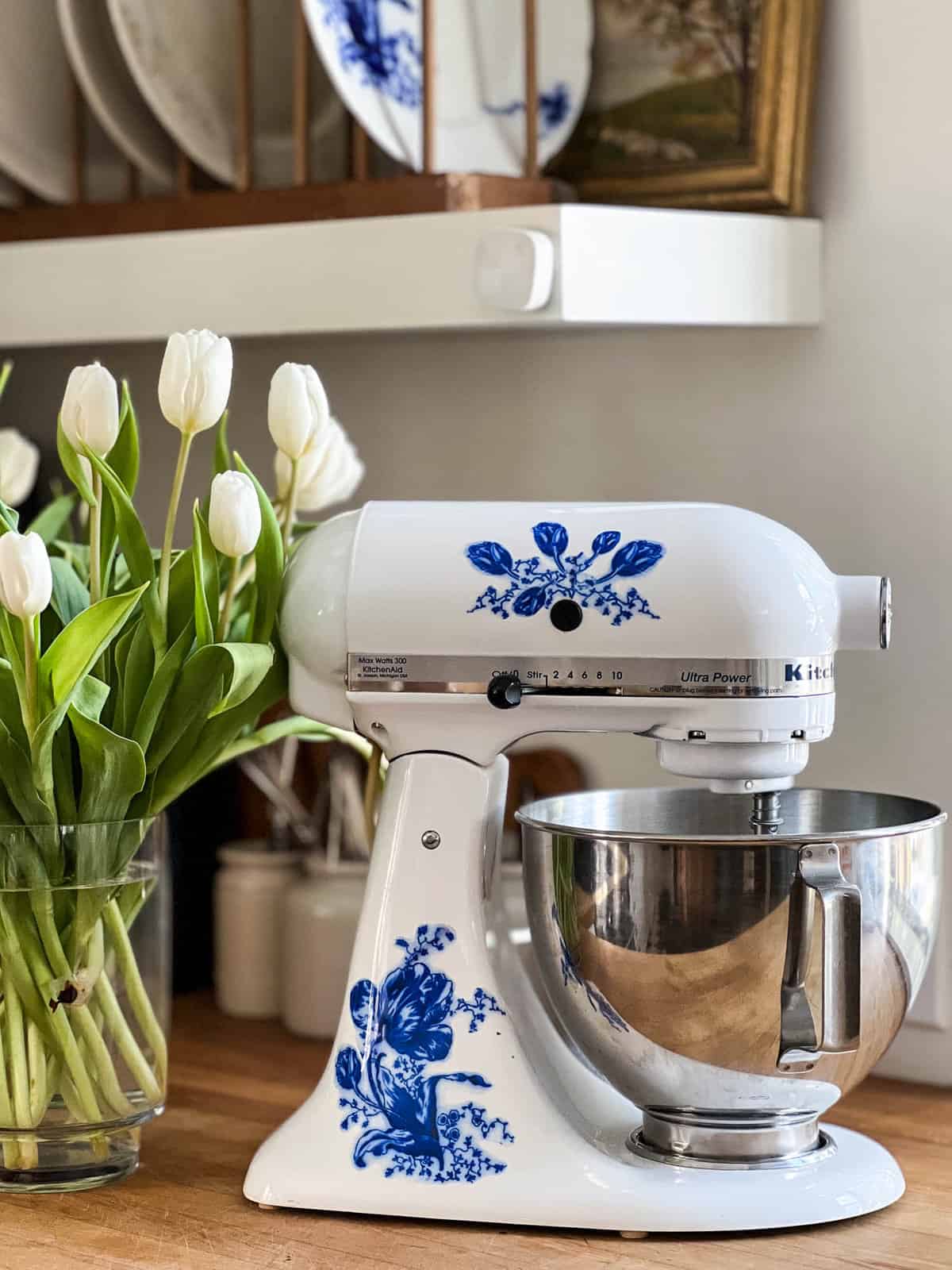 Kitchen Aid stand mixer with blue and white tulip decal beside a vase of white tulips.
