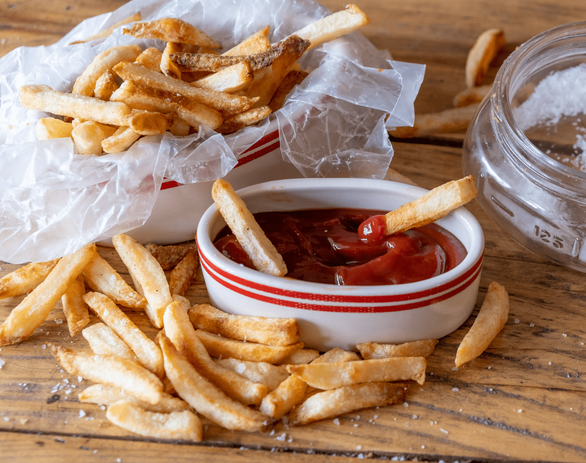 Frozen french fries made from scratch with lots of salt and a bowl of ketchup for dipping.