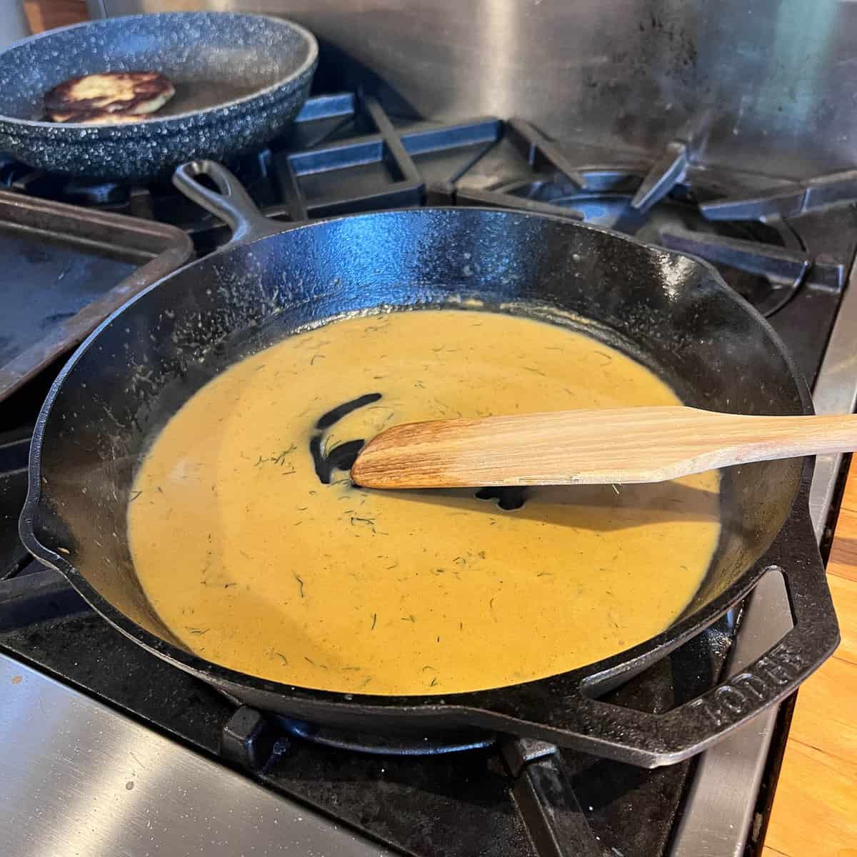 Chicken gravy with dill in cast iron pan with wood spoon.