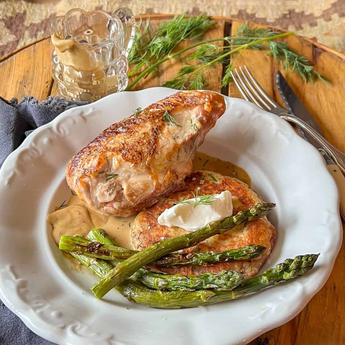 Sour cream pan sauce with chicken , potato pancakes and asparagus on ironstone plate.
