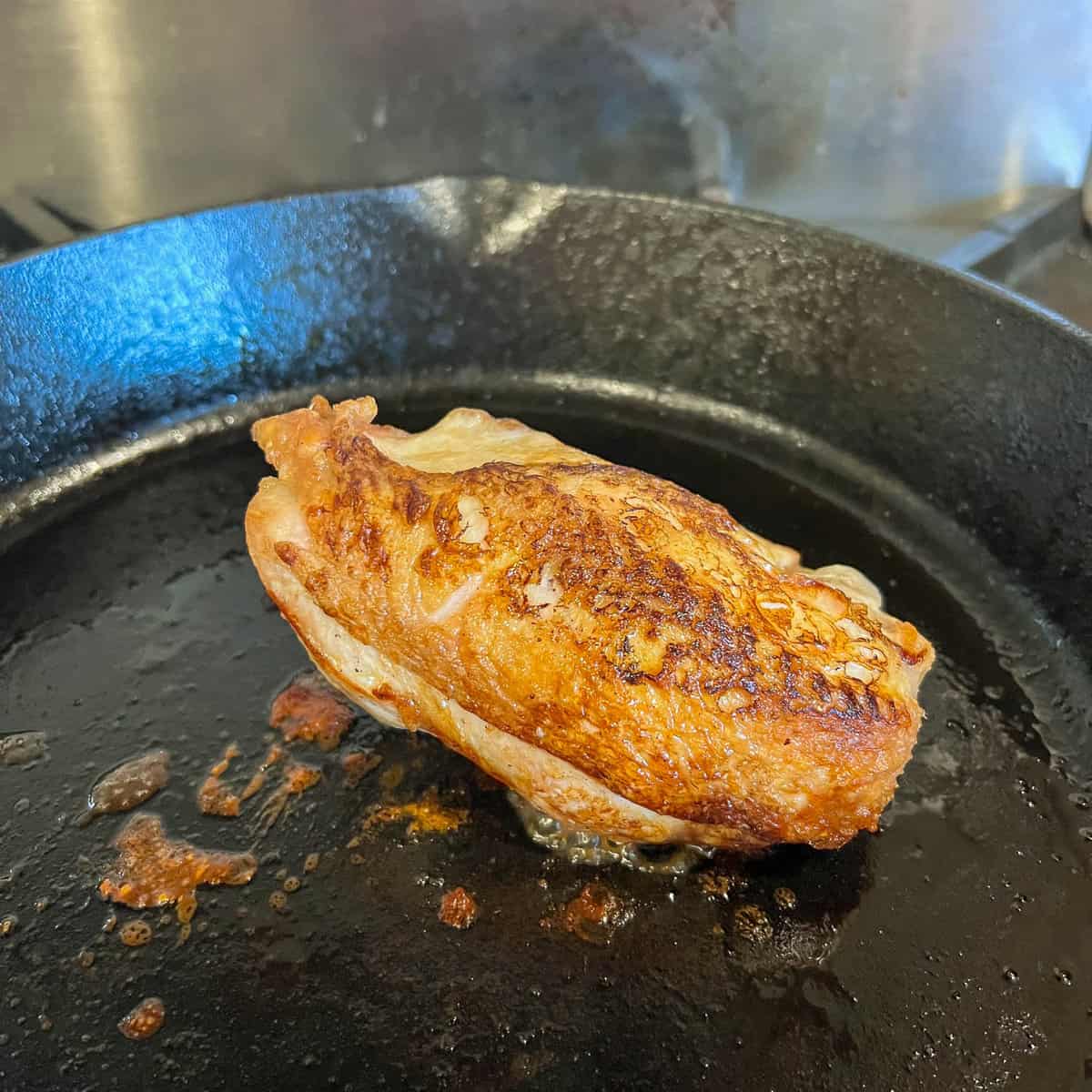 Chicken breast cooking in cast iron skillet.