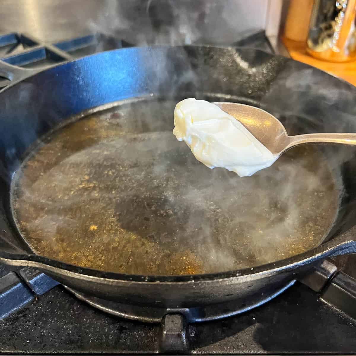 Sour cream about to be added to sour cream sauce in cast iron pan.