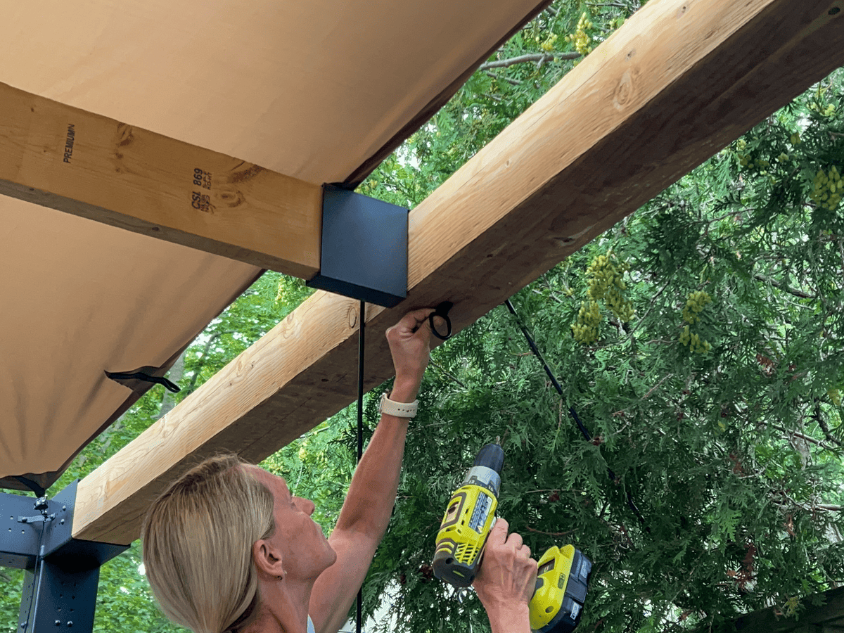 Screwing D ring onto underside of top beam on pergola.