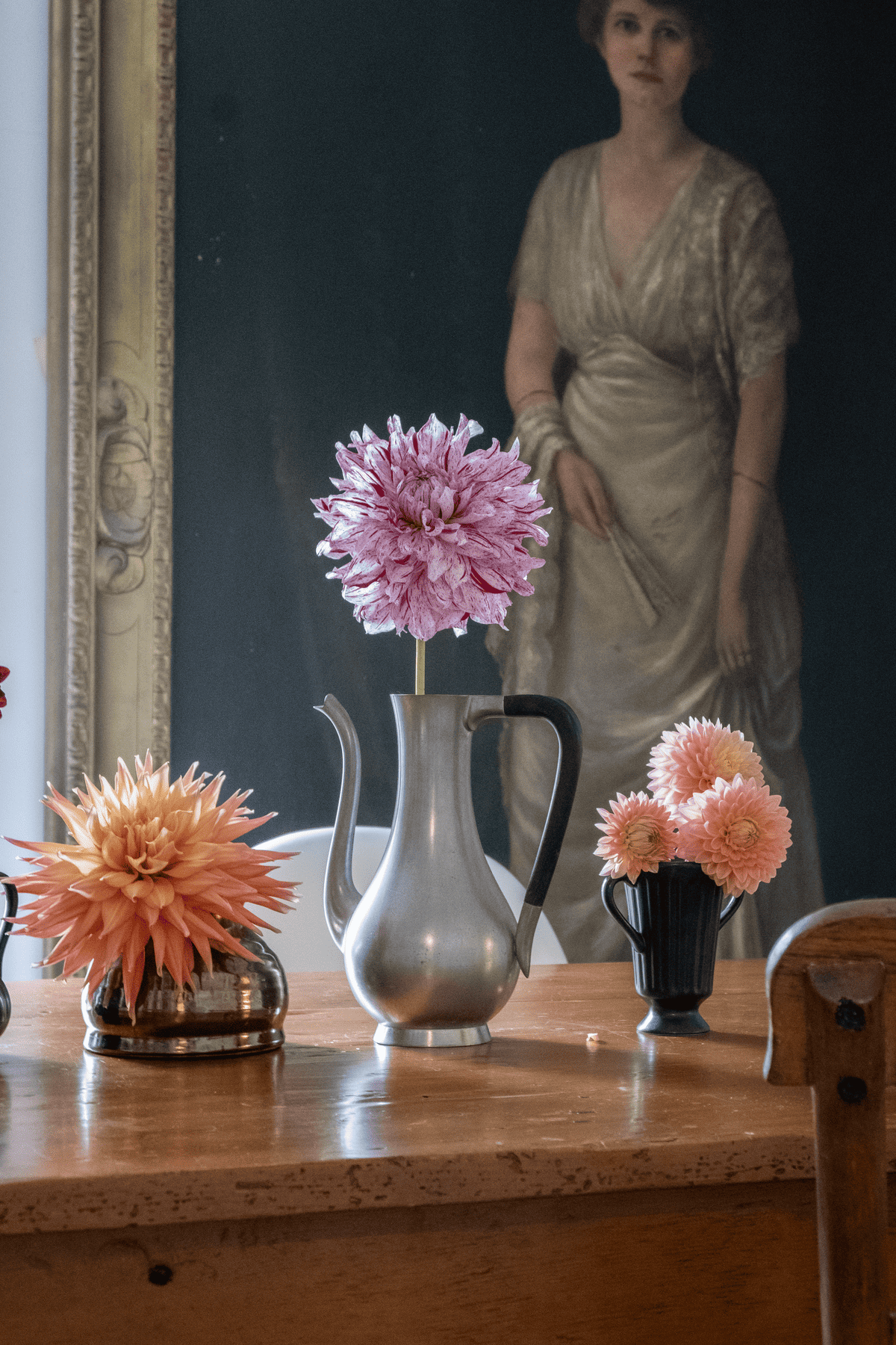 Alfred C, AC Paint and Hamilton Lillian dahlias in different vases in front of life sized portrait with gold frame.