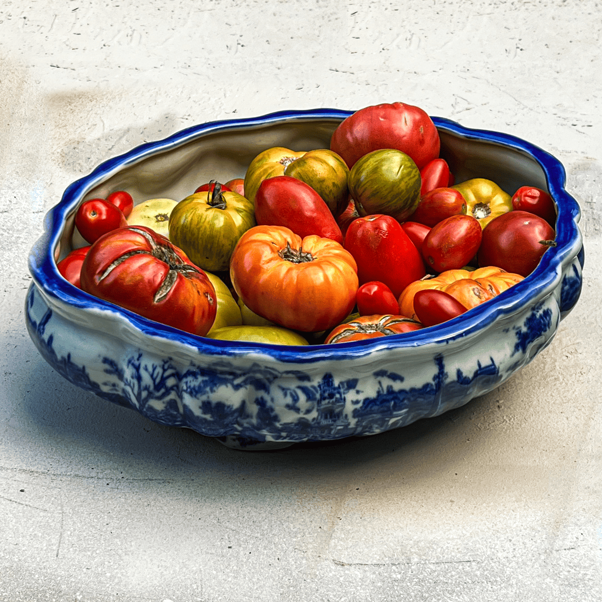 A flow blue bowl filled with colourful heirloom tomatoes of different colours and shapes.