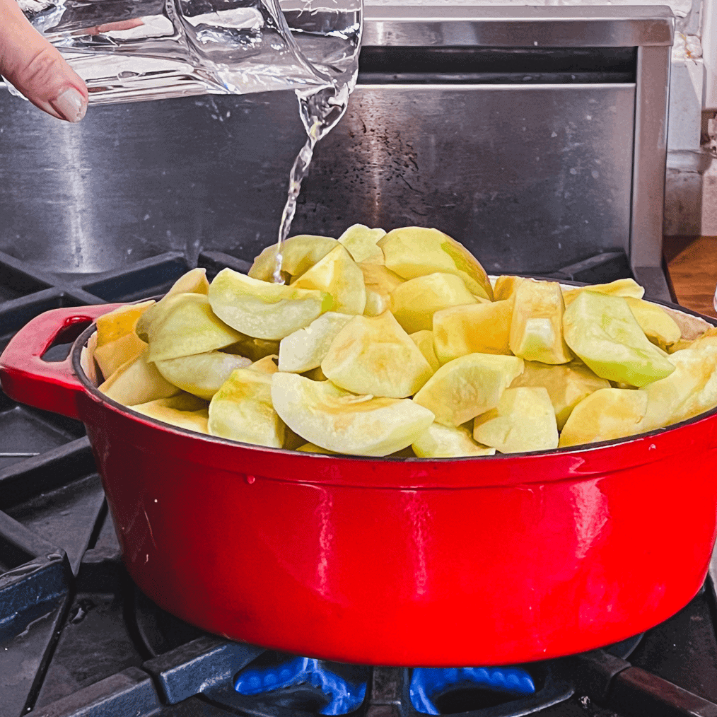 Pouring water into pot of chopped apples to prevent burning.