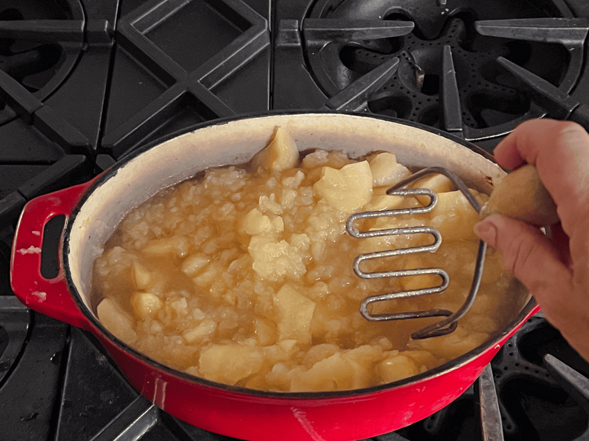 Cooked apples in an enamel dutch oven being mashed.