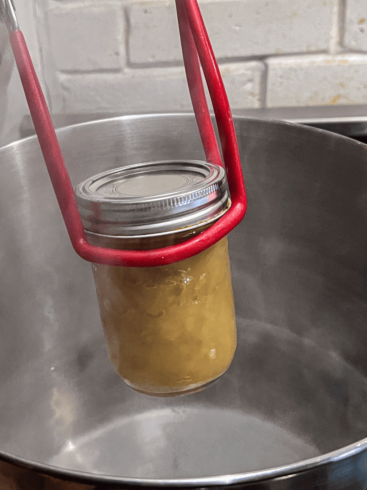 Mason jar being placed into water bath with red tongs.
