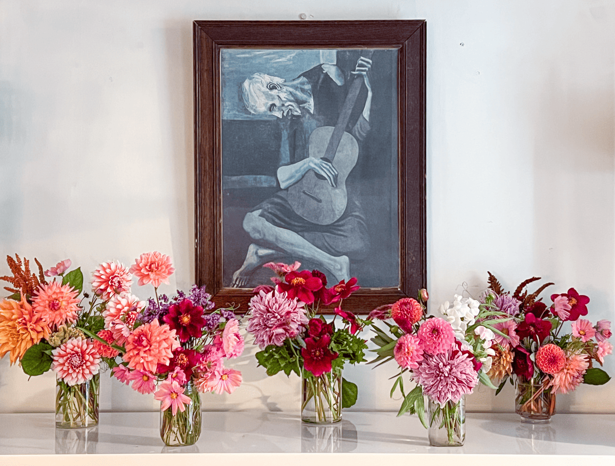 Five colourful flower arrangements on a white buffet with Picasso's The Old Guitarist hanging on the wall behind.