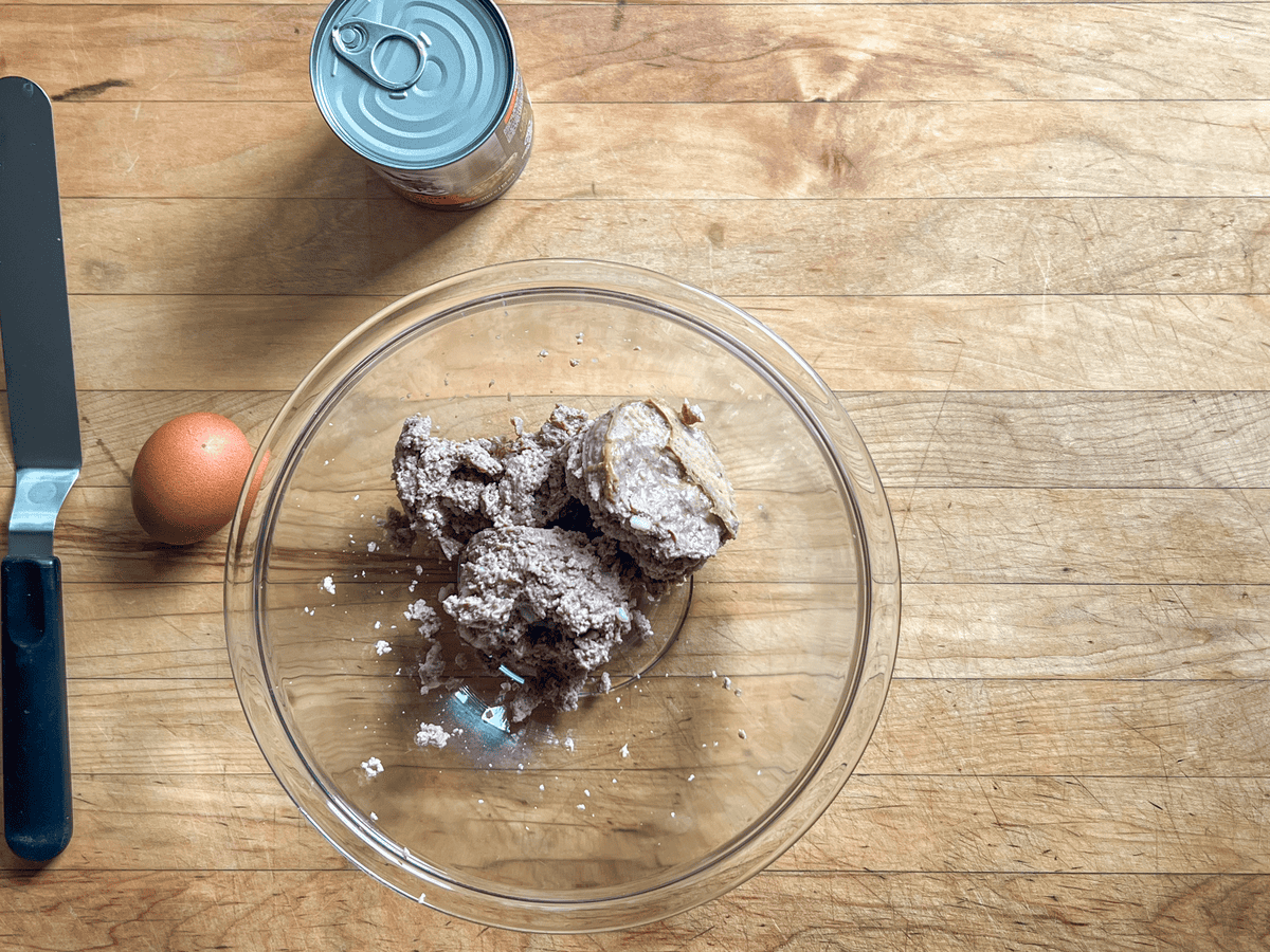 Canned dog food dumped into a bowl with an egg and offset spatula to the side.