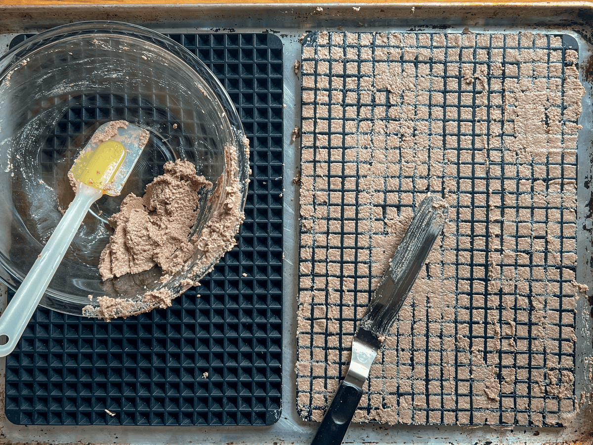 Pyramid baking sheets being filled with wet dog food treat mixture, pushed in by offset cake spatula.